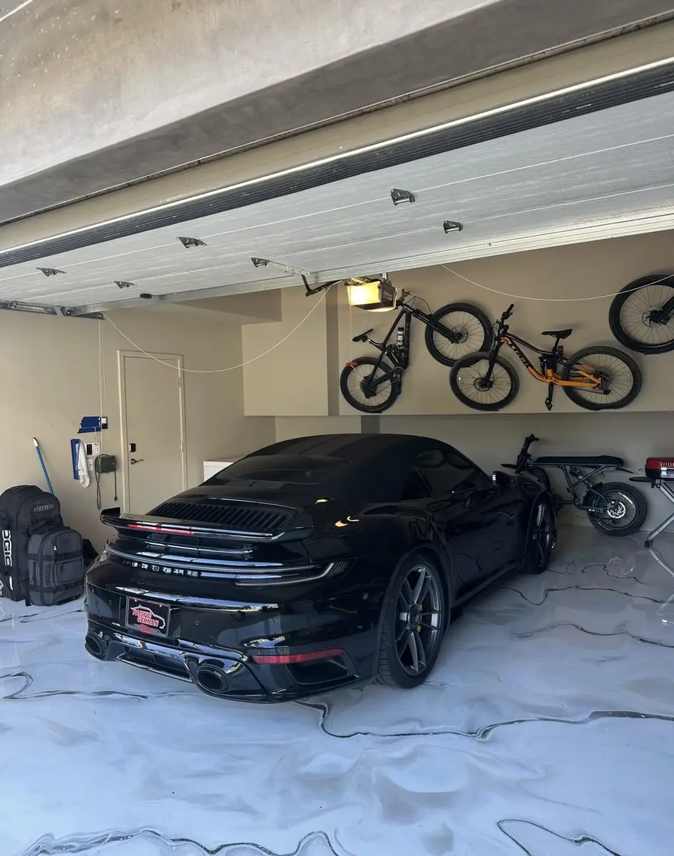 Black Porsche parked on a pearl-white metallic epoxy garage floor, finished by Epoxy Dept